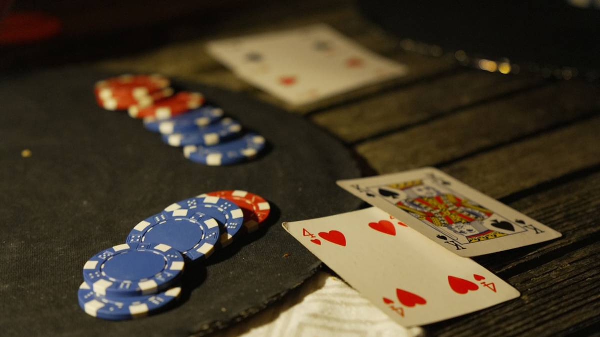 Tumpukan chip poker dan kartu remi di atas meja gelap